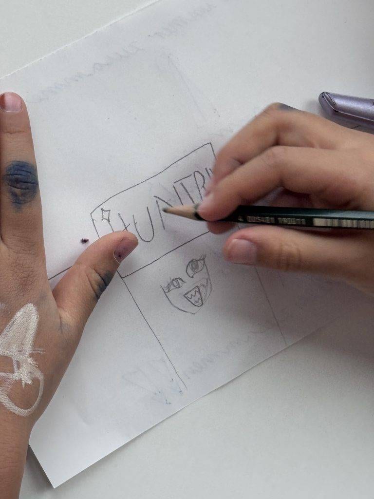 die hände eines kindes zeichnen mit einem bleistift auf weißes papier. die zeichnung scheint ein gesicht unter dem wort hunter zu sein. auf der linken hand und den fingern des kindes sind kritzeleien zu sehen.