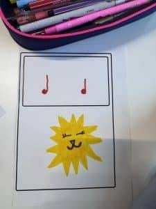 Klasse ¾, immer donnerstags ein blatt papier zeigt oben in einem kasten zwei rote musiknoten und unten in einem kasten die zeichnung einer lächelnden, zwinkernden gelben sonne mit einem niedlichen gesicht. am oberen rand des bildes sind rosa stifte und ein federmäppchen zu sehen.