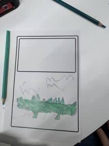 Klasse ¾, immer donnerstags die zeichnung eines kindes auf einem arbeitsblatt zeigt unten einen grünen, stacheligen dinosaurier oder drachen und darüber berge und formen. auf dem weißen tisch sind zwei grüne bleistifte und ein teil einer federmappe zu sehen.