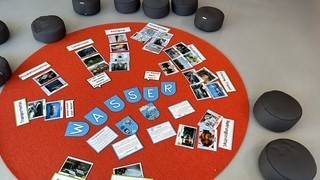 Unser Wasser-Projekt ein runder orangefarbener teppich, auf dem das wort wasser in blauen karten geschrieben steht, umgeben von verschiedenen fotos und textkarten. graue kissen sind im kreis um den teppich angeordnet.